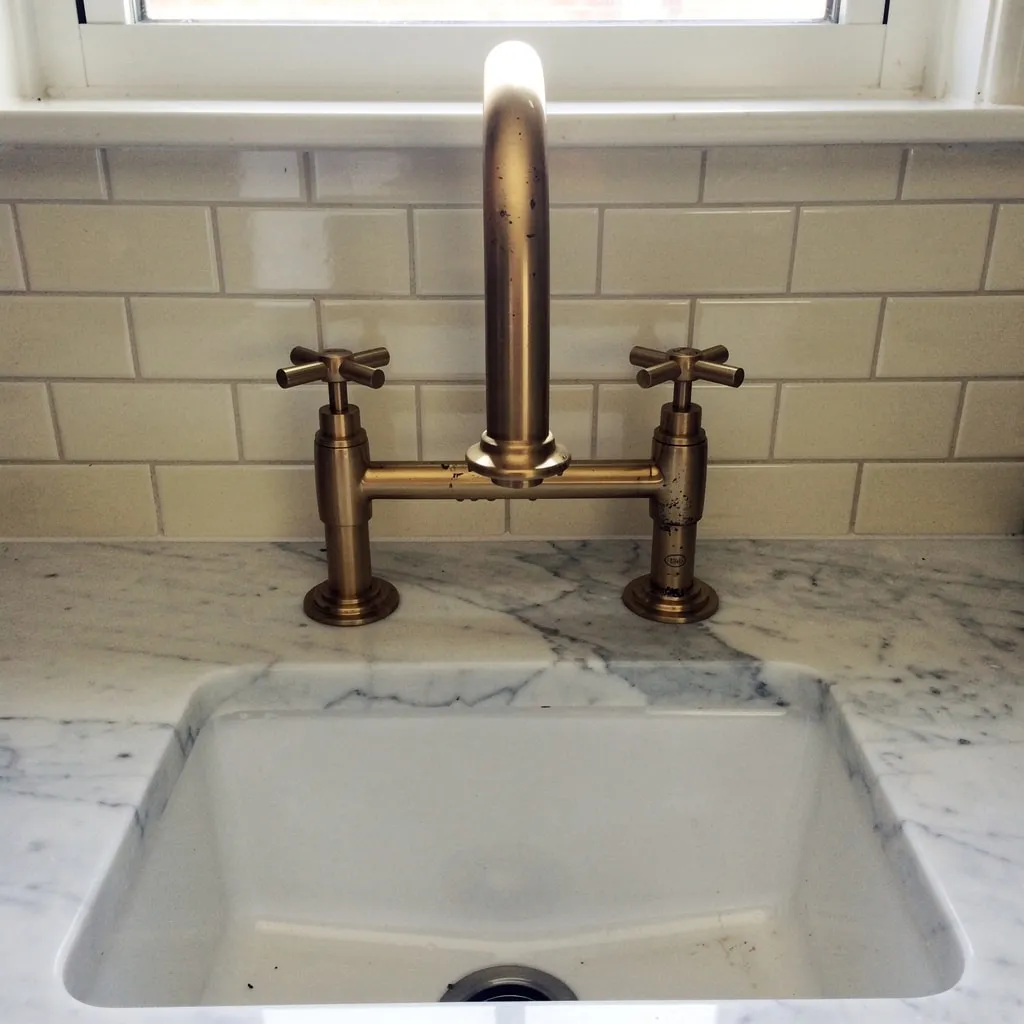 Polished brass bridge faucet on thick marble, set against classic ivory subway tile.